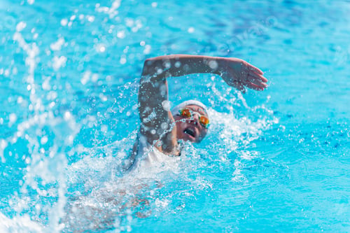 Preview: Female swimmer in white swim cap and goggles performing freestyle stroke in an outdoor pool