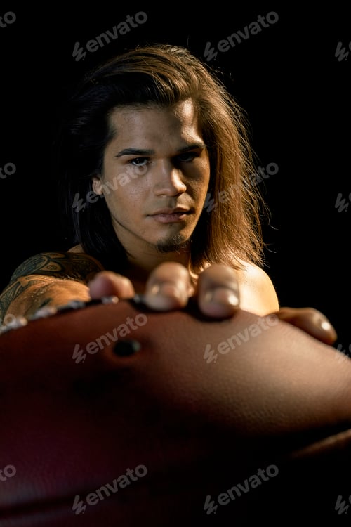 Preview: Portrait of bare chested young man with football, black background
