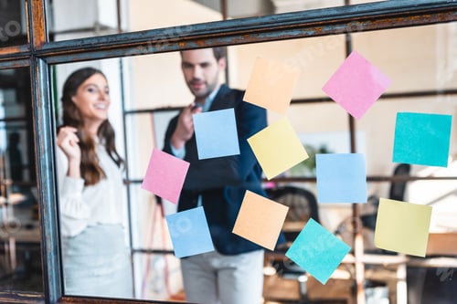 Preview: close-up view of colorful sticky notes and smiling business colleagues working behind in office