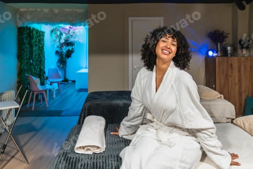 Preview: Beautician smiling, wearing bathrobe, sitting on massage table in beauty spa