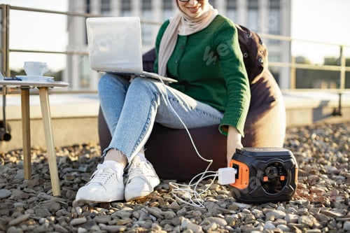 Preview: Lady connecting laptop to power supply via cord outdoors