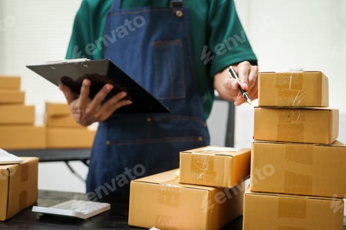 Preview: A man is working at his desk, preparing parcel boxes for shipment. He checks packs items carefully