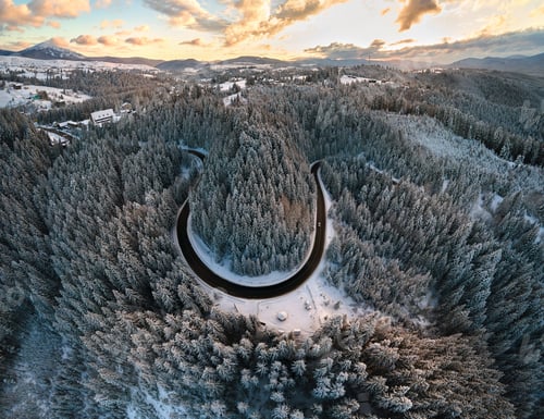 Preview: Aerial view of winter landscape with snow covered mountain hills and winding forest road in morning.