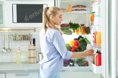 Preview: Woman taking bottle with milk out of refrigerator in kitchen