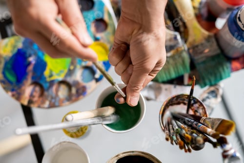 Preview: Hands of painter holding paintbrush over glass of water while cleaning it