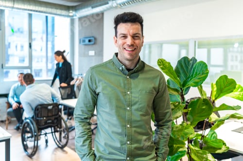 Preview: Confident businessman smiling in modern inclusive office with disabled colleagues working