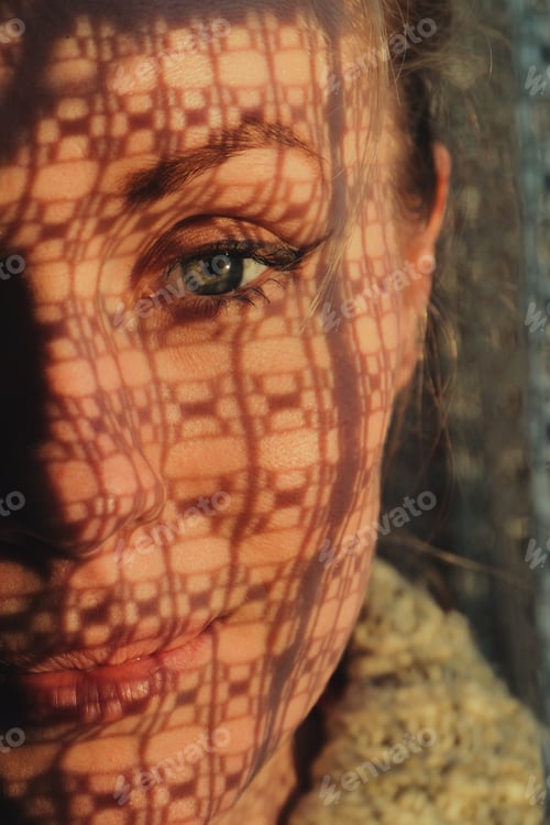 Preview: portrait of a woman standing next to a window, sunset through curtain cast a shadow on her face