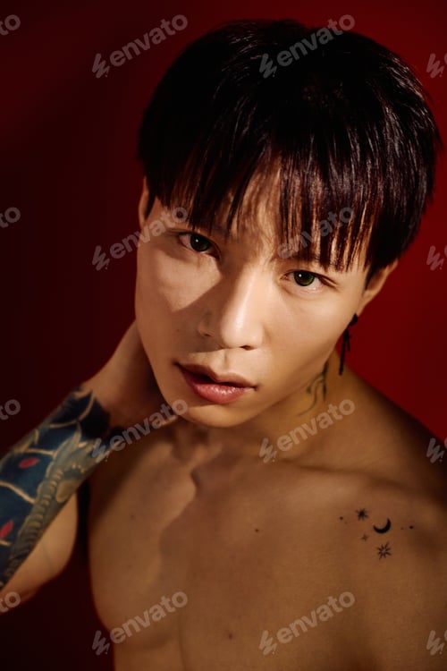 Preview: Stylish young Asian man confidently poses against a soft lit vibrant red backdrop