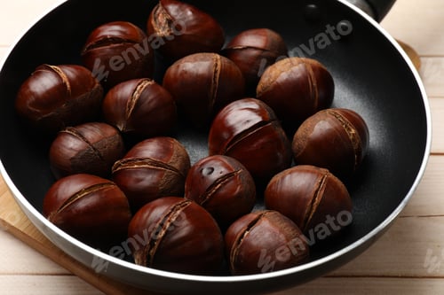 Preview: Roasted edible sweet chestnuts in frying pan on wooden table, closeup
