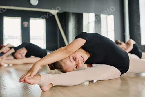 Preview: Flexible smiling girl in ballet dancing attire practicing stretching exercises