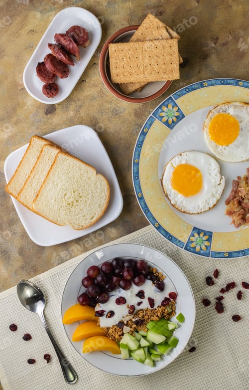 Preview: Overhead shot of a breakfast spread composed of eggs, fruits, bread, biscuits and sausage
