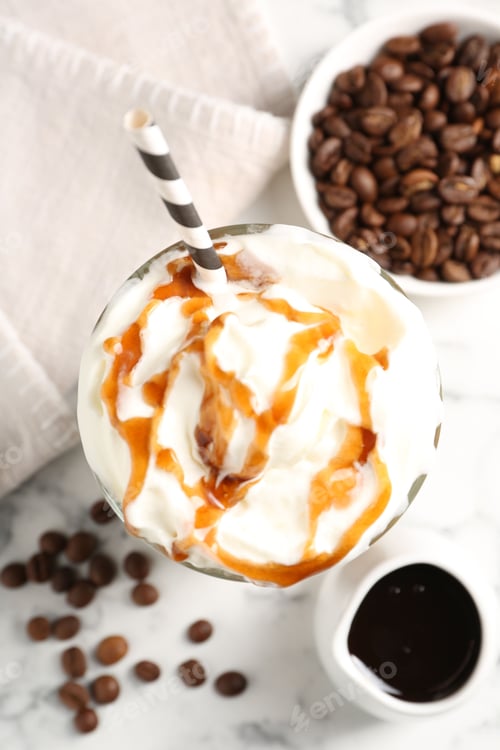 Preview: Tasty iced coffee with whipped cream, syrup and beans on white marble table, flat lay