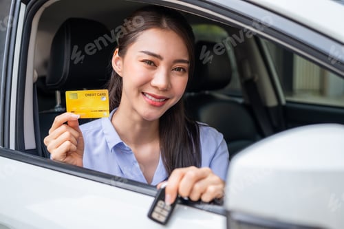 Preview: Portrait of Asian woman driver holding credit card while sitting in car.