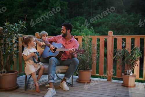 Preview: Young African american man enjoys playing the guitar with little children accompaining him with