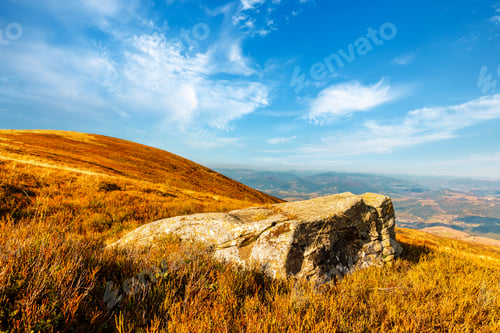 Preview: Big old stone lies on grassy hill in highland under blue sky