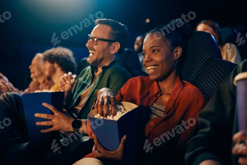 Preview: Happy black woman eating popcorn while watching movie at cinema.