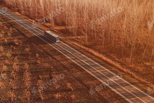 Preview: Semitrailer eighteen-wheeler truck on the road through deciduous forest landscape in autumn sunset