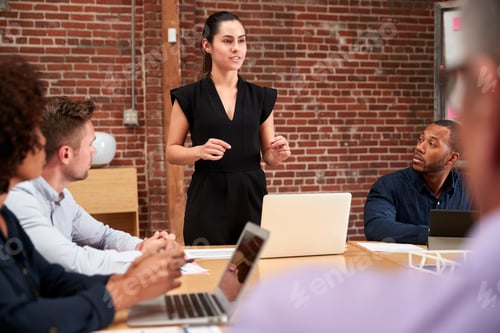 Preview: Young Businesswoman Standing And Leading Office Meeting Around Table