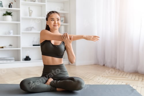 Preview: Smiling asian woman in yoga wear performing seated arm stretch exercise