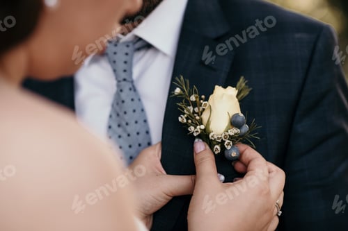 Preview: Closeup shot of the bride putting a white flower in the suit pocket of the groom