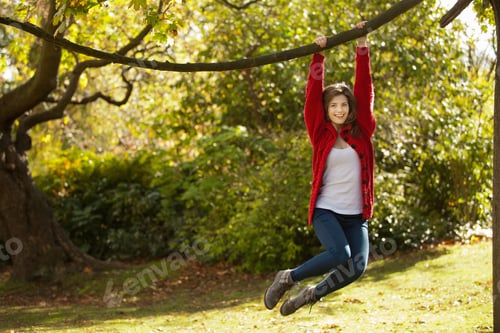Preview: Teenage girl swinging from tree in park