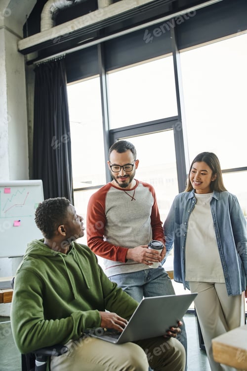 Preview: young african american businessman sitting with laptop near positive asian woman and bearded man