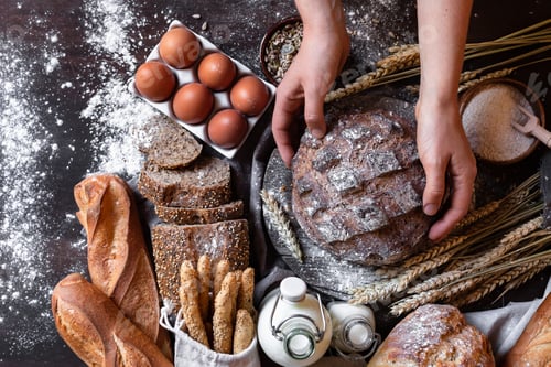 Preview: Young woman holding freshly baked dark round bread in her hands.