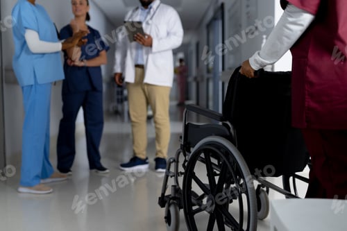 Preview: African american female doctor walking with wheelchair in corridor at hospital