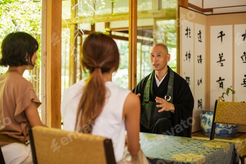Preview: Two Japanese women and Buddhist priest kneeling in Buddhist temple, talking.