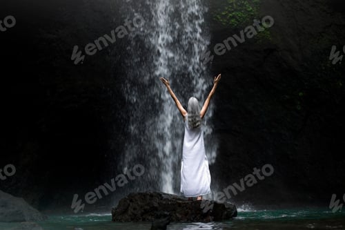 Preview: Beautiful senior woman standing in front of a tropical waterfall
