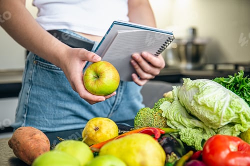 Preview: Woman with notepad and vegetables on the kitchen table preparing a recipe.