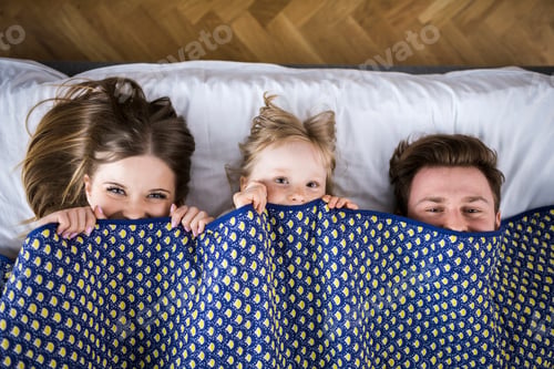 Preview: Happy family lying in bed, hiding under blanket