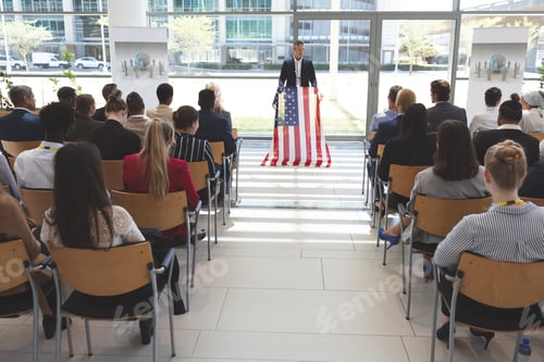 Preview: Mixed race man speaker speaking in a business seminar in office building with american flag