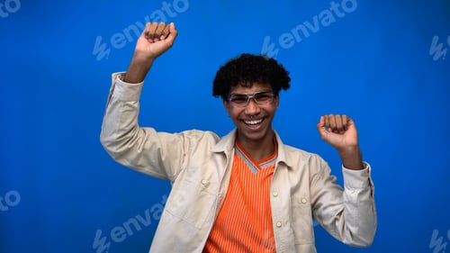 Preview: Cheerful african american man in eyeglasses showing yes gesture on blue background