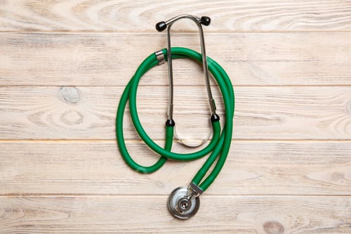Preview: Top view of green stethoscope on yellow wooden background. Medical examination concept