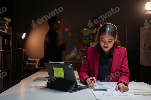 Preview: Focused asian accountant woman working late at night in office using calculator to calculate company