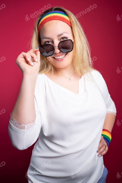 Preview: Joyful LGBT woman adjusting sunglasses ad smiling at camera against burgundy background