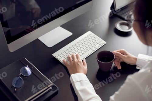 Preview: Businesswoman holding coffee cup and working with laptop computer in the office.