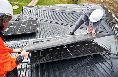 Preview: Technicians carrying photovoltaic solar module while installing solar panel system on roof of house