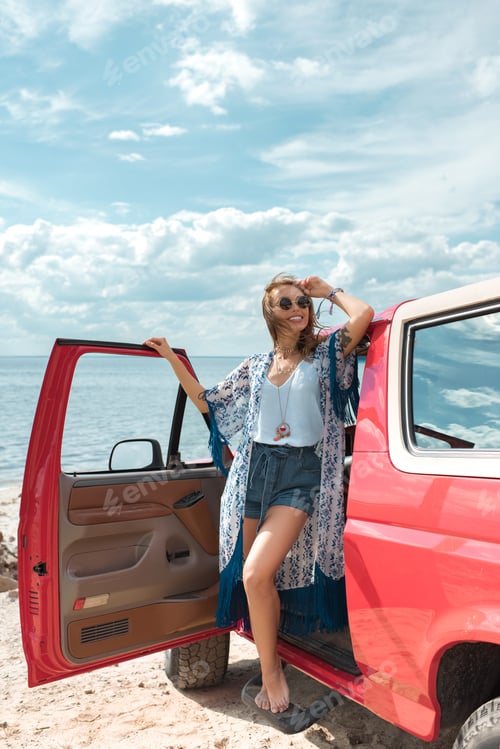 Preview: happy young woman in sunglasses standing near red car