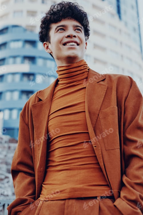 Preview: Stylish young man in a brown turtleneck and suit, smiling confidently against an urban cityscape