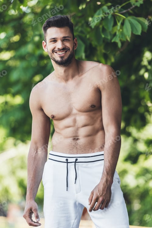 Preview: happy shirtless young man looking at camera in front of green leaves