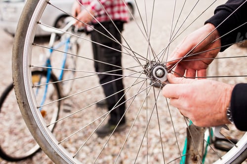 Preview: Cropped image of senior man repairing bicycle tire with son working in background