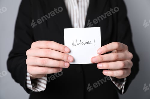 Preview: Human resources manager holding sticky note with word Welcome on grey background, closeup