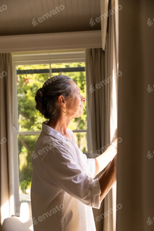 Preview: Opening curtains, mature woman enjoying sunlight at home, looking outside