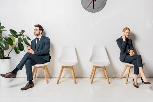 Preview: young businessman and businesswoman holding paper cups and waiting on chairs in line