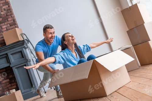Preview: Happy young couple having fun with cardboard boxes in new house at moving day