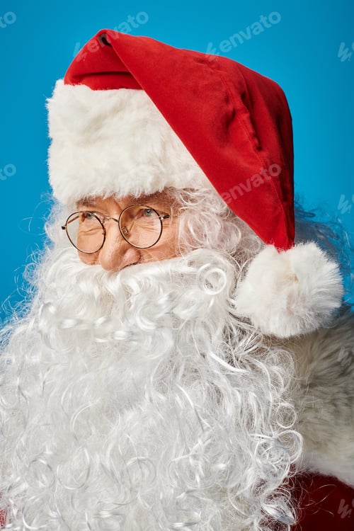 Preview: portrait of happy Santa Claus with white beard and eyeglasses looking away on blue background