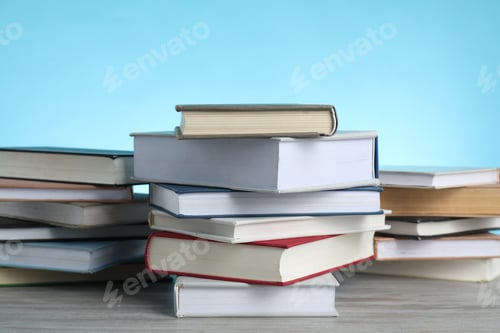Preview: Many stacked books on wooden table against light blue background, closeup