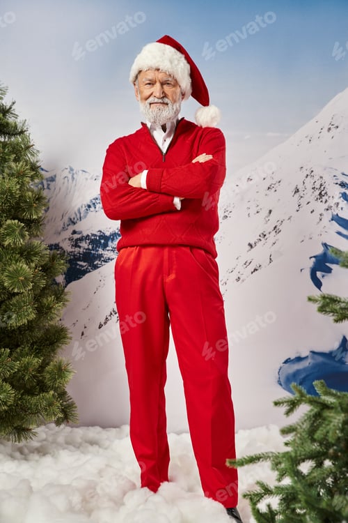 Preview: handsome Santa in red costume and hat looking at camera with crossed arms on chest, winter concept